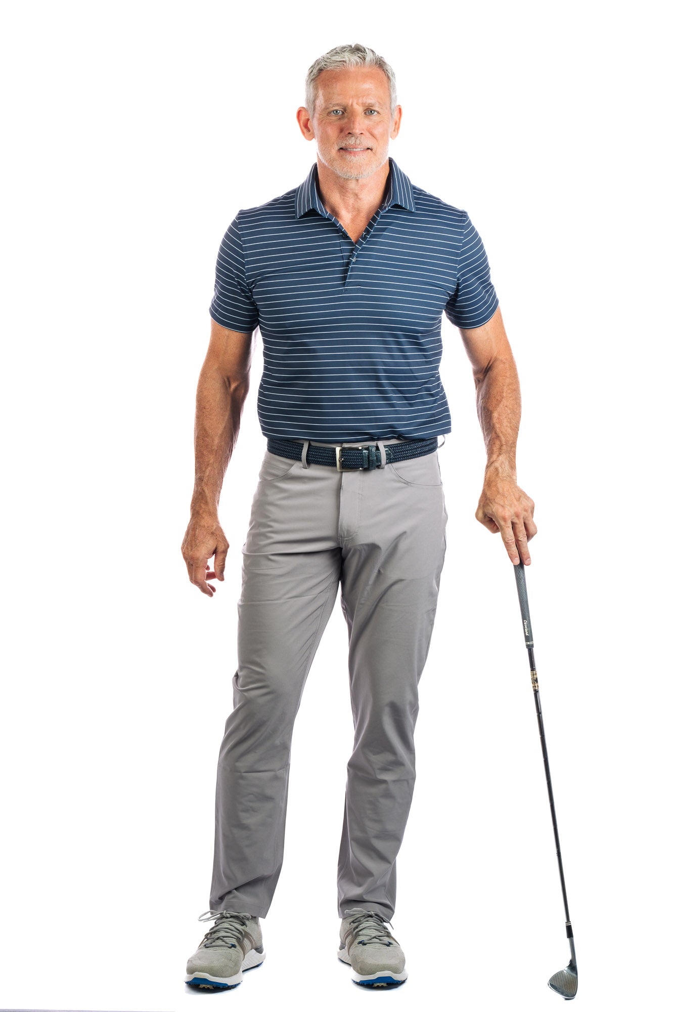A model posing in a navy striped golf polo and grey pants, holding a golf club.