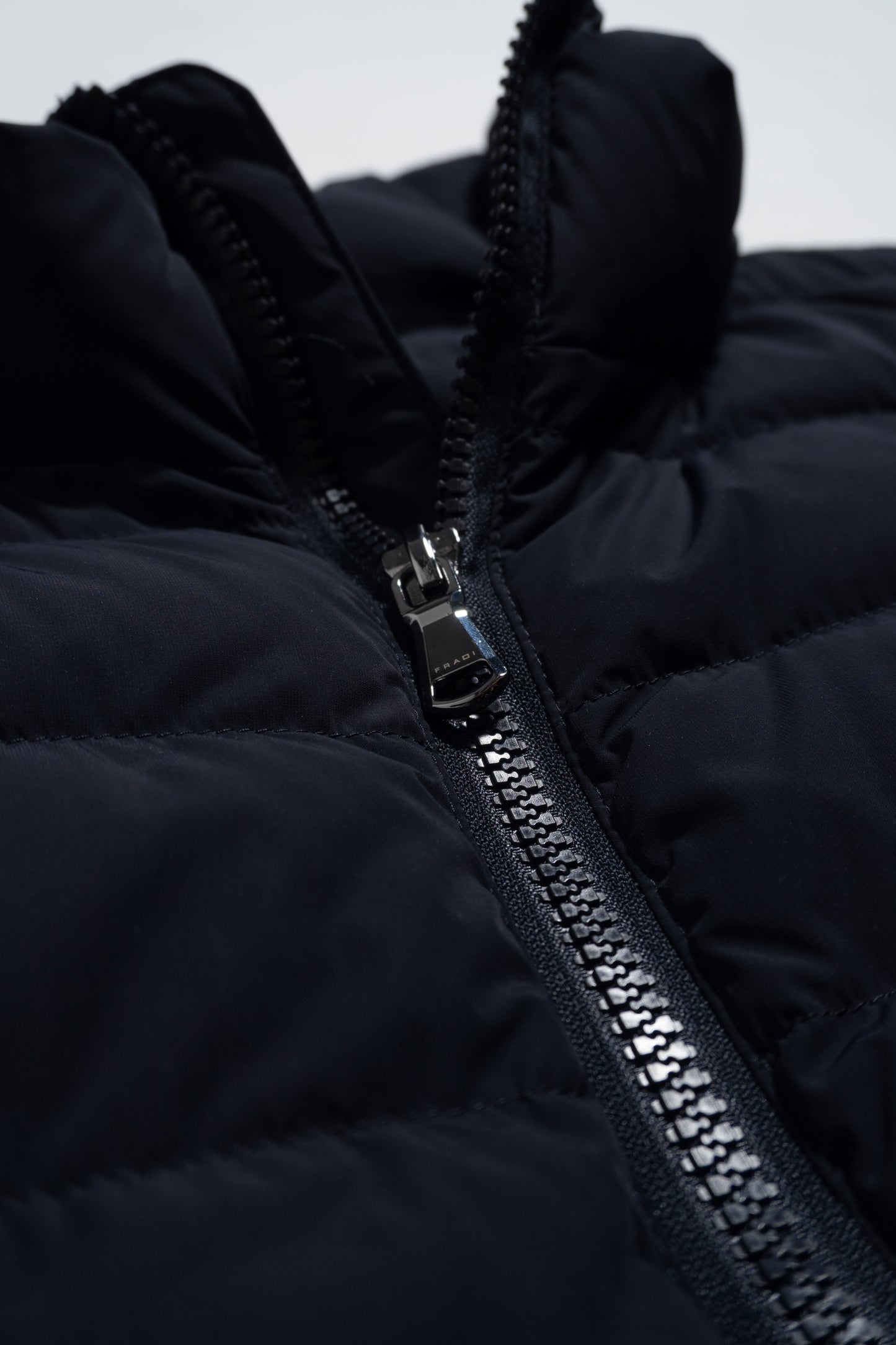 Close-up of a black quilted jacket featuring a shiny silver zipper partially unzipped, with visible stitching and puffy fabric texture.