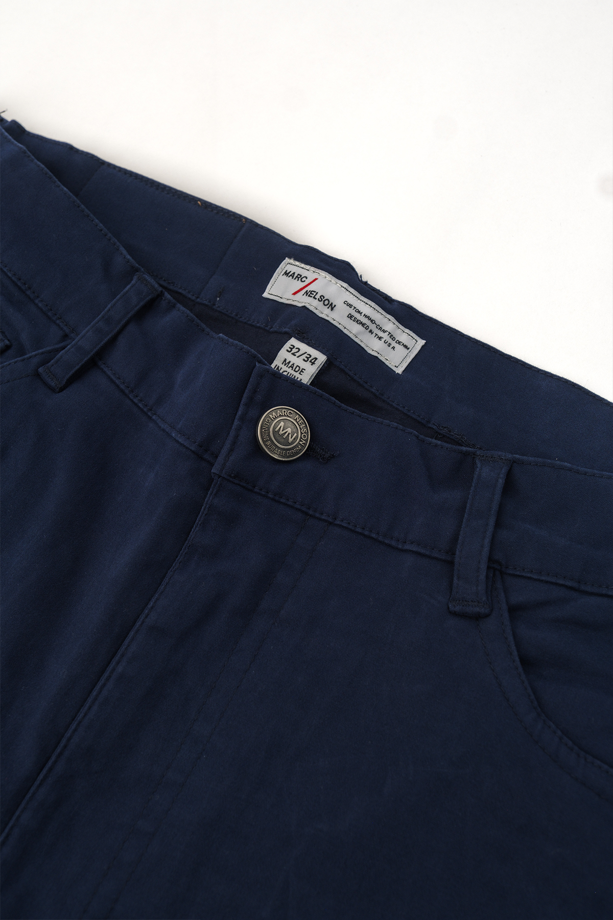 Close up photo of the frontside of the George Navy Pants focusing on the details of the button and the waist tag. 