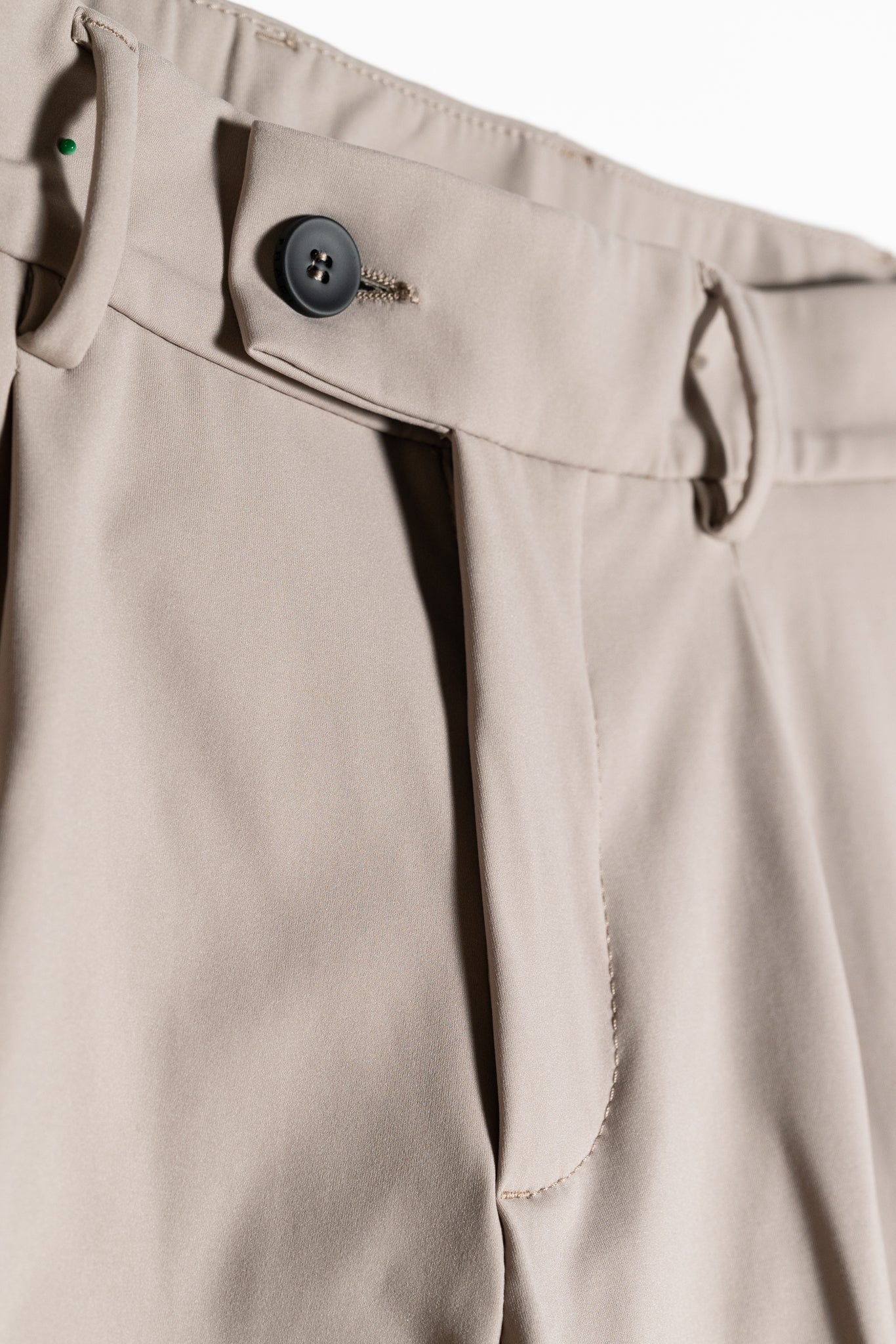 Close-up of beige dress pants featuring a button closure, belt loops, pleats, and smooth fabric texture.