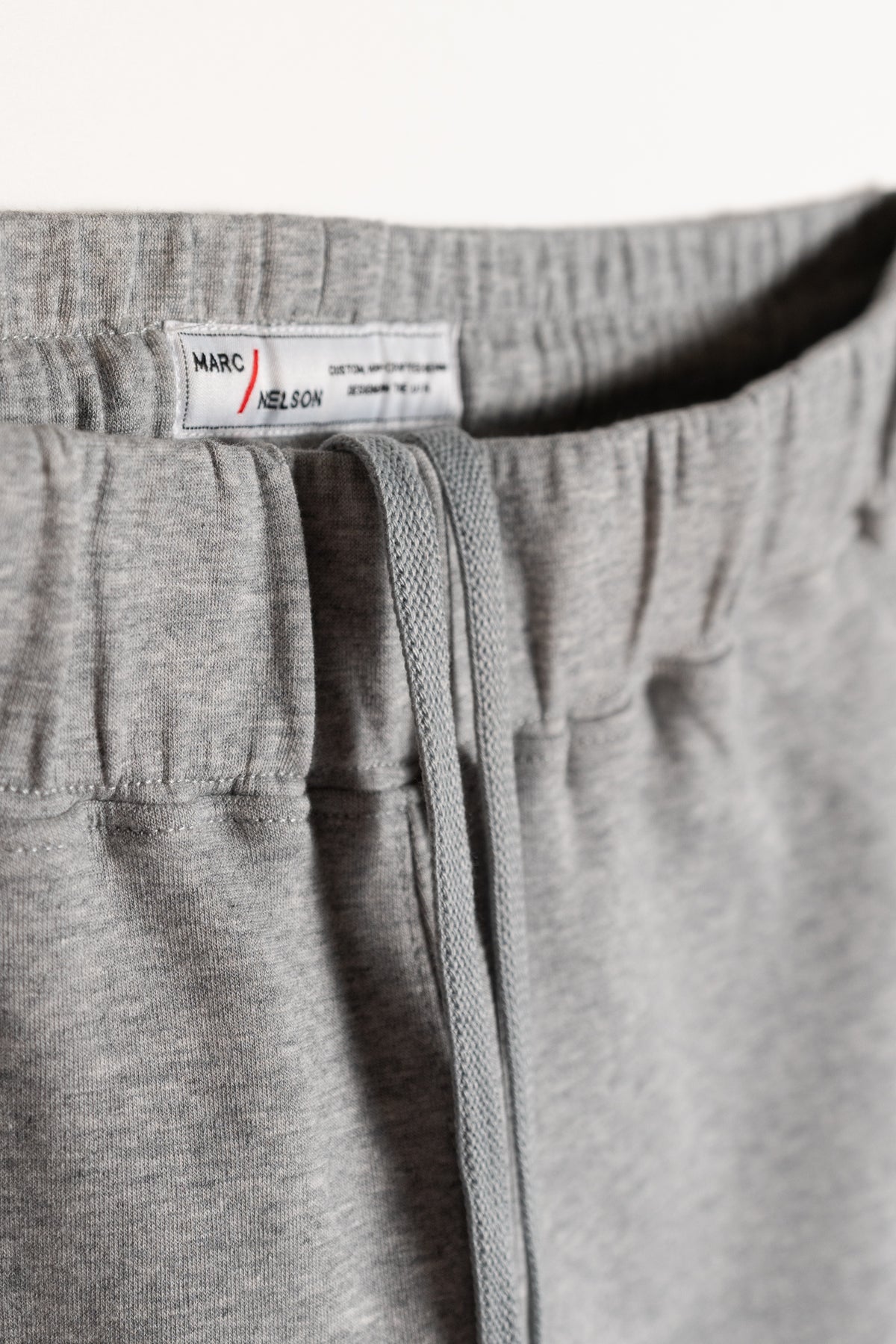 Close-up of the waistband of light gray sweatpants with a drawstring and a visible white clothing label that reads Marc Nelson. The fabric appears soft and comfortable.