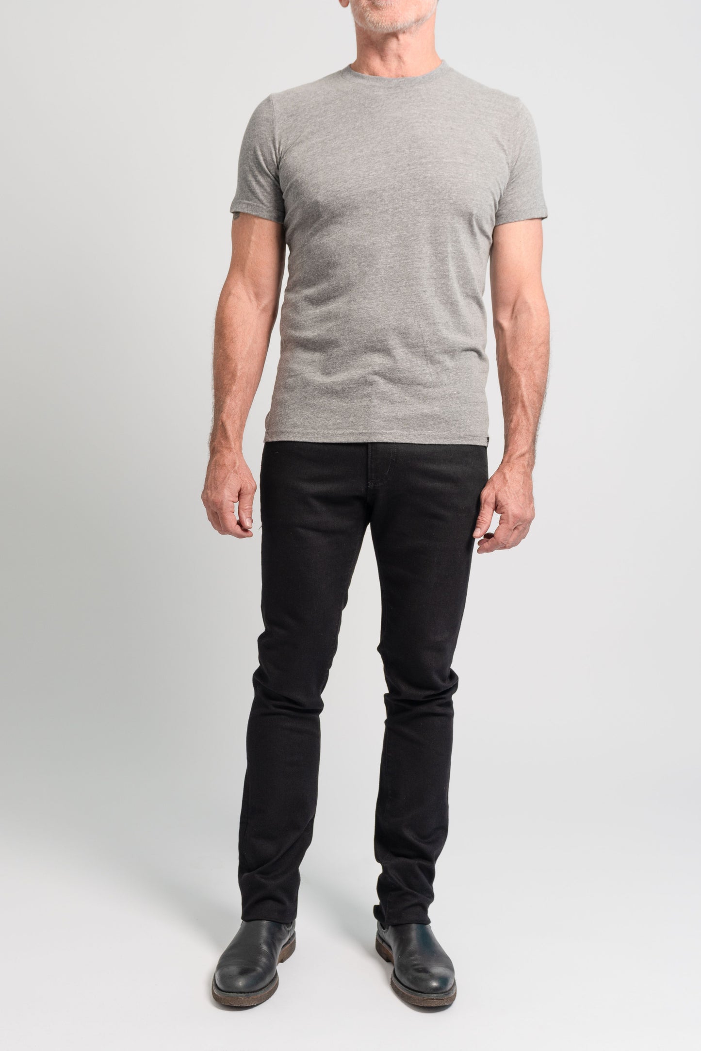 Full length photo of model wearing black denim and grey t shirt on a white background.