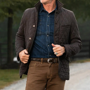  Man wearing a brown quilted jacket, denim shirt, and brown pants.