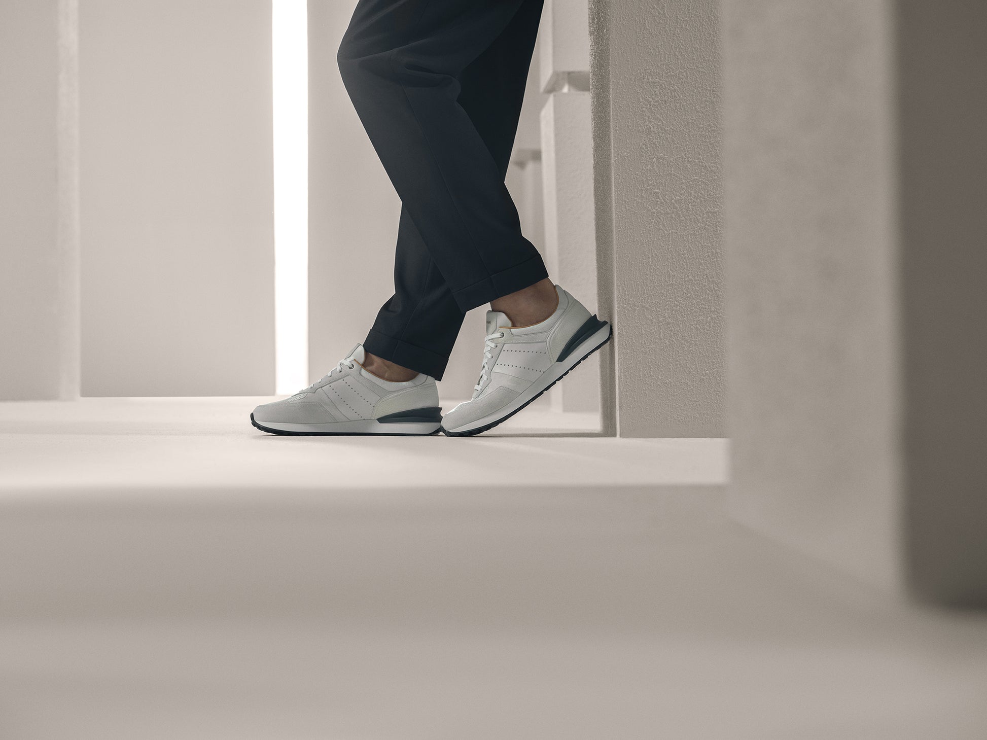 Person wearing white sneakers and black pants standing next to a wall.