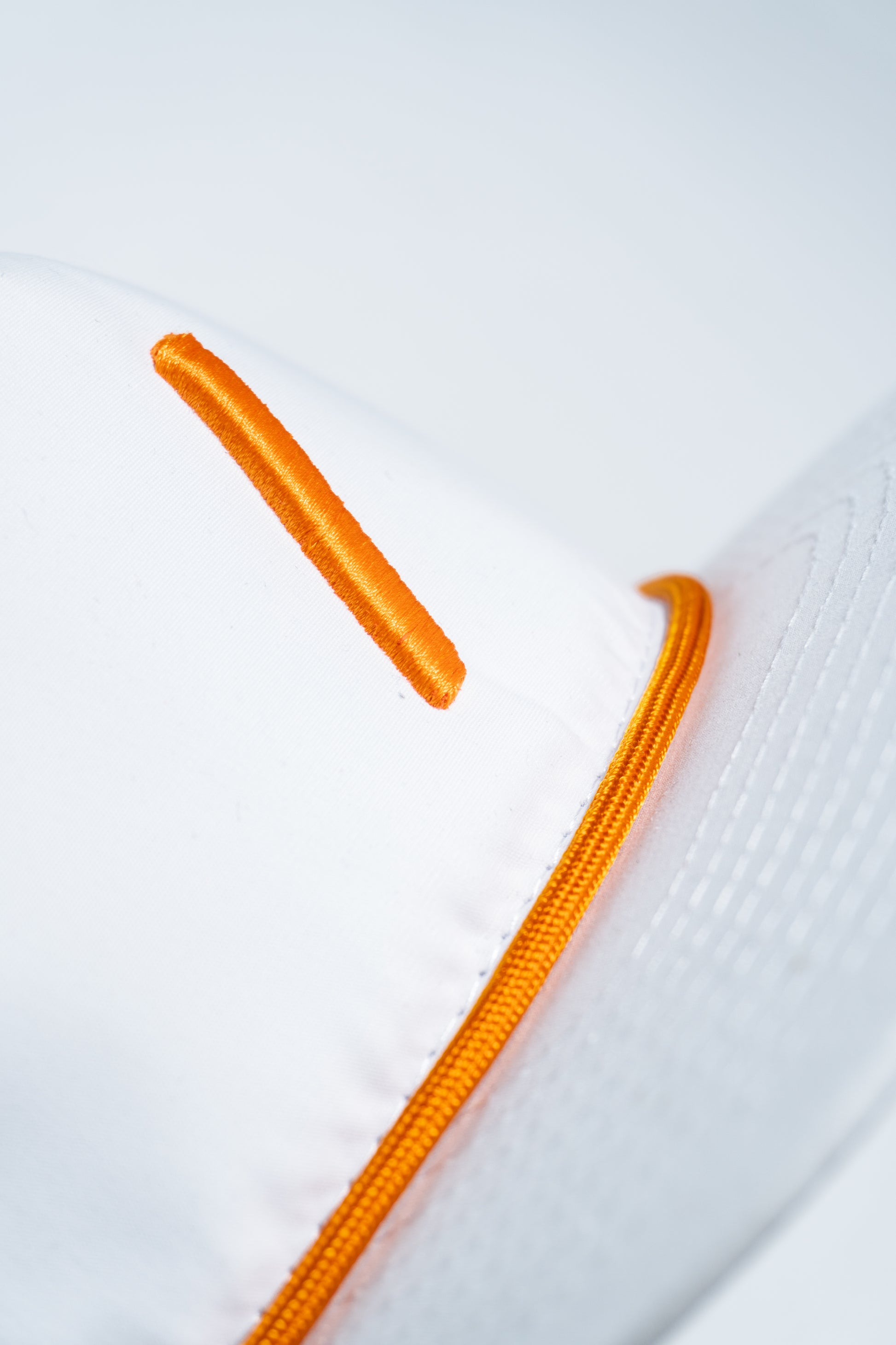 Close-up of a white cap featuring an orange embroidered line and orange piping along a seam, with part of the visor visible on the right side.