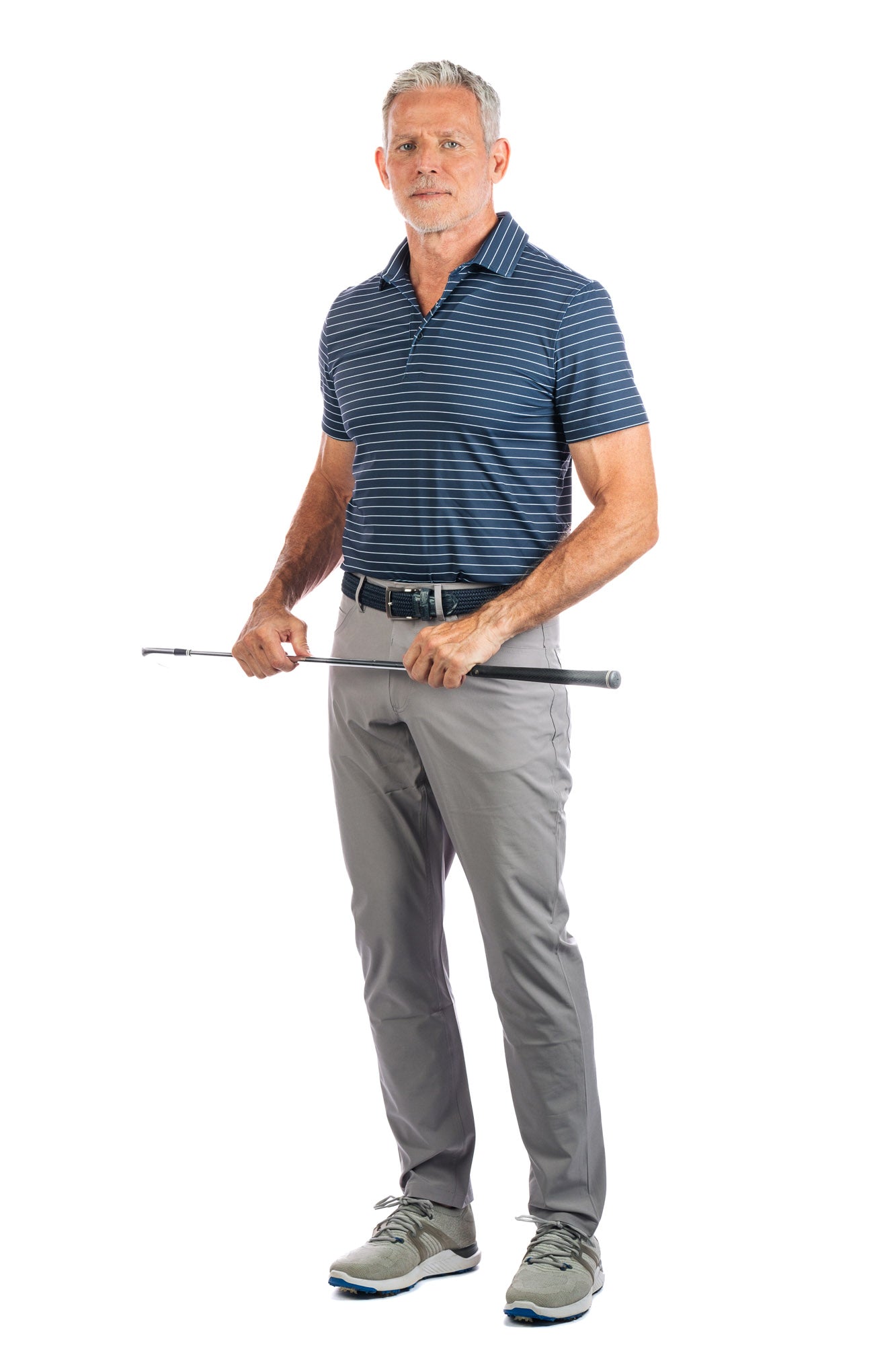 A model posing in a navy striped golf polo and grey pants, holding a golf club in both hands.