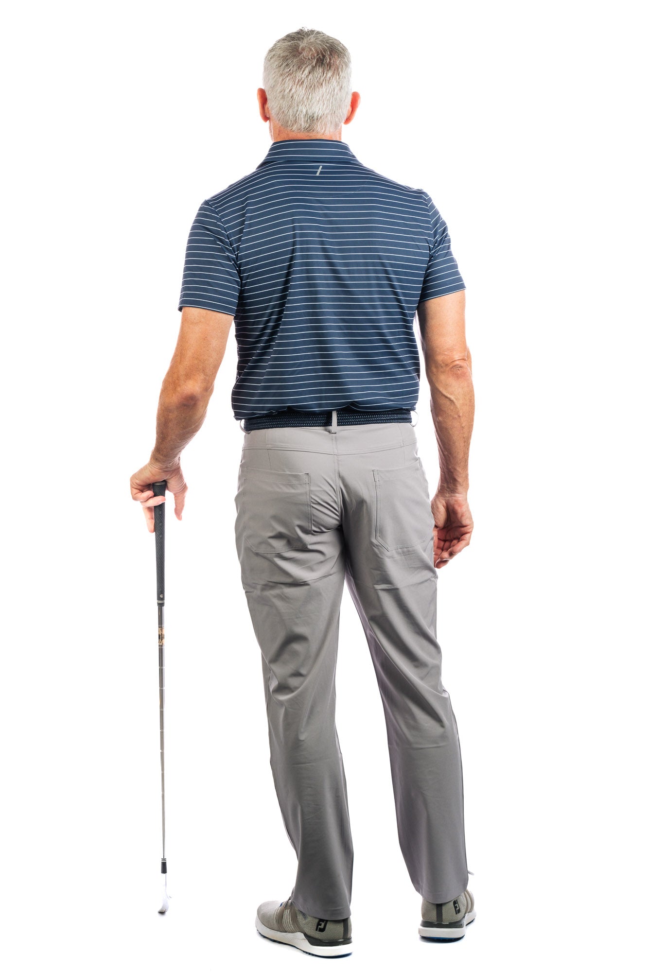 Back view of a model posing in a navy striped golf polo and grey pants, holding a golf club.