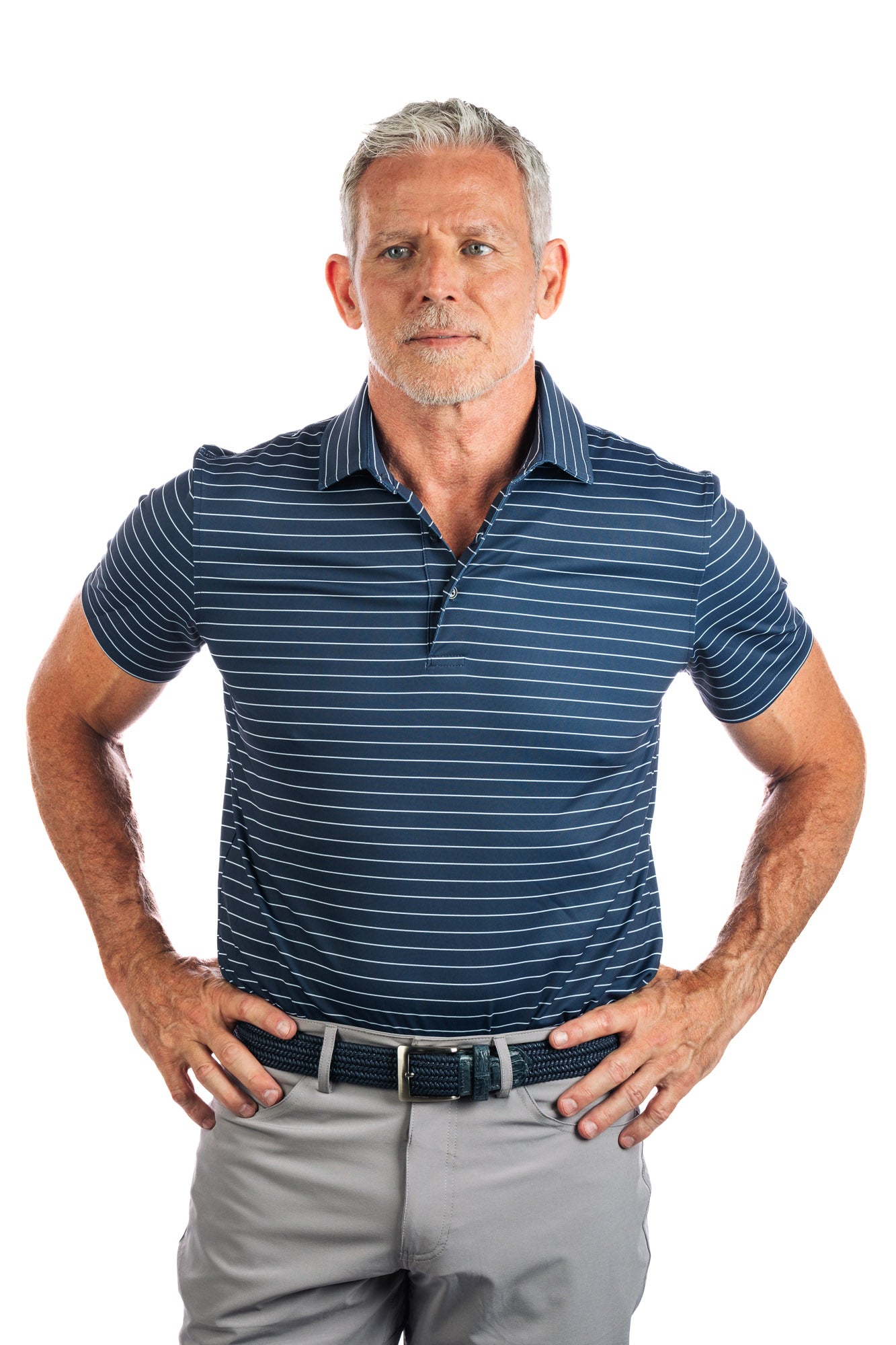 Frontal photo of model wearing navy polo with white stripes on a white background with his hands on his hips. 