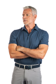  A model wearing a navy striped golf polo, grey pants, and a belt.