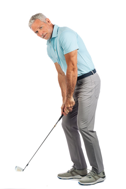 Photo of model wearing light blue golf polo and concrete golf pants facing the camera holding a golf club. 