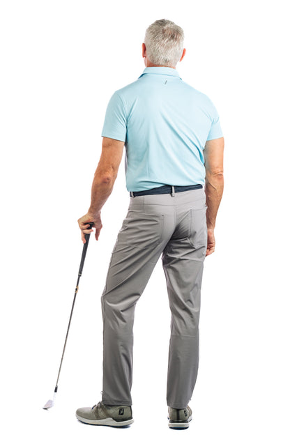 Backside of model posing with golf club wearing a light blue golf polo and concrete golf pants. 