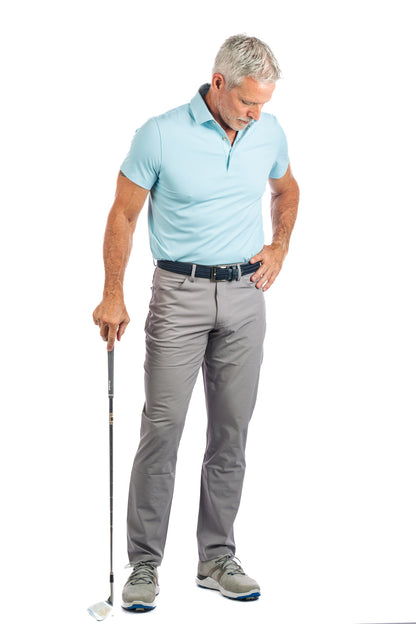 Frontside photo of model wearing light blue golf polo and concrete golf pants looking at the ground.