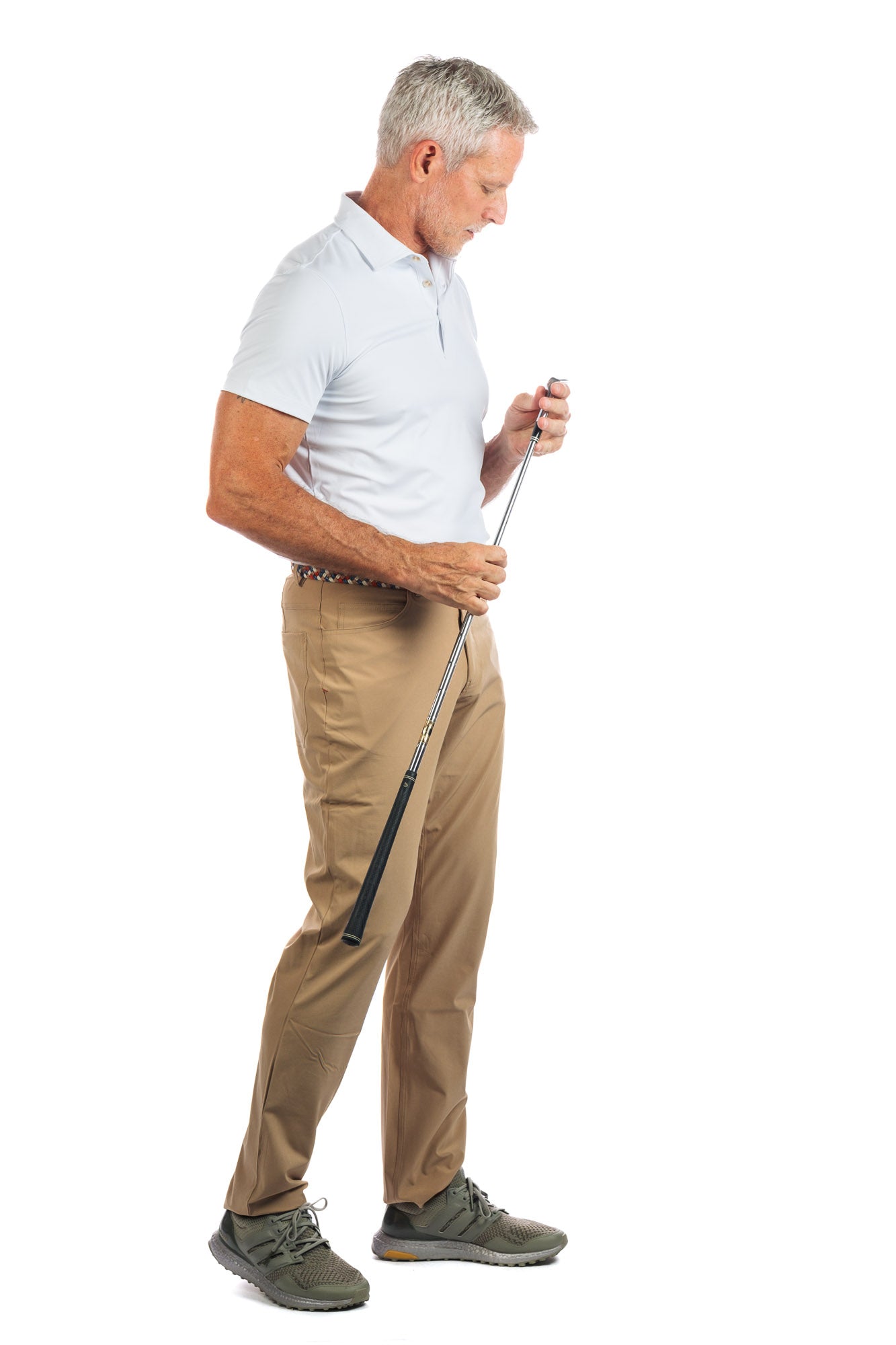 Photo of a model wearing our White Golf Polo on a White Background looking down at a golf club. 