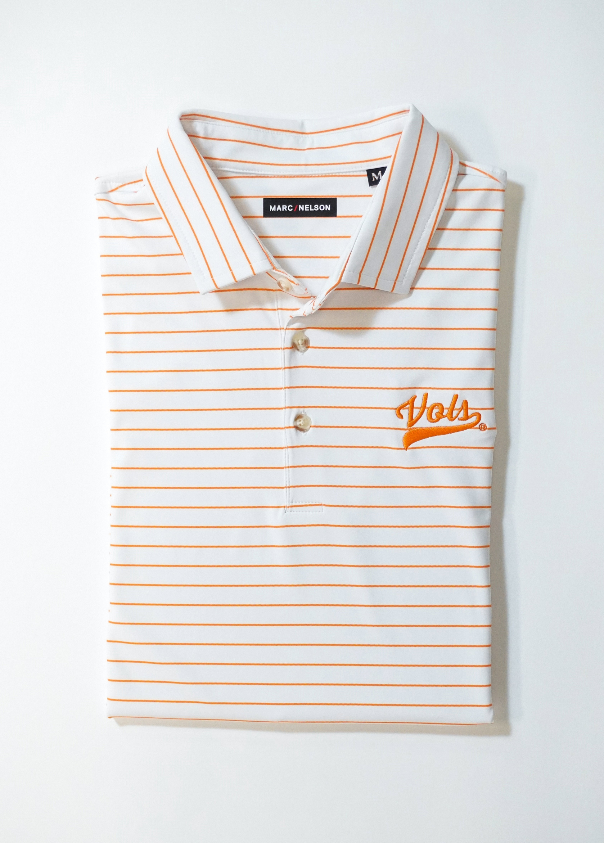 A neatly folded white polo shirt with thin orange horizontal stripes, a collar, and Vols embroidered in orange on the left chest. The shirt tag reads Marc Nelson.