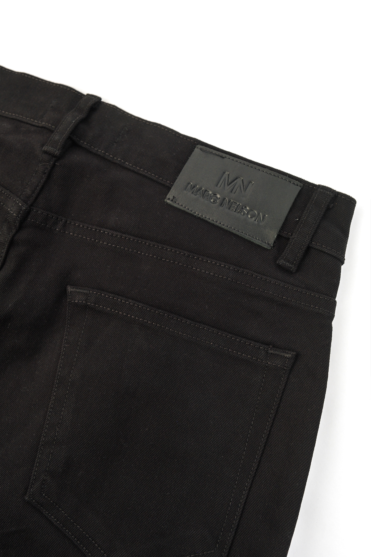 Close up photo of the backside of black denim displaying the leather tag and pockets. 