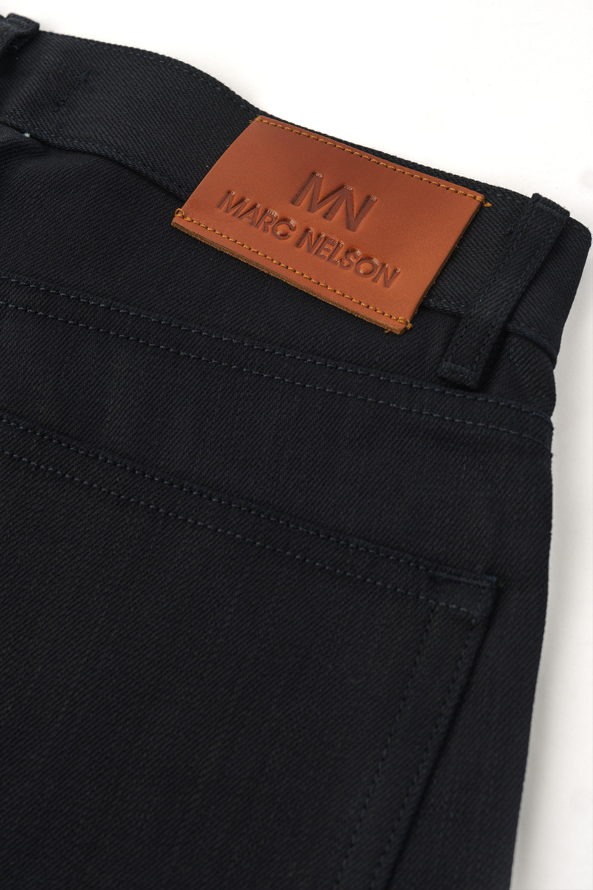 Close up photo of Kaihara blue stitch denim on white background showing the back pocket and back tab. 