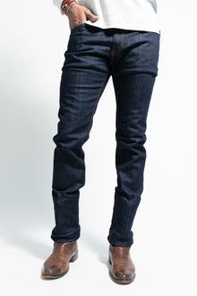  Man in slim straight dark wash jeans and brown boots standing on a white background.